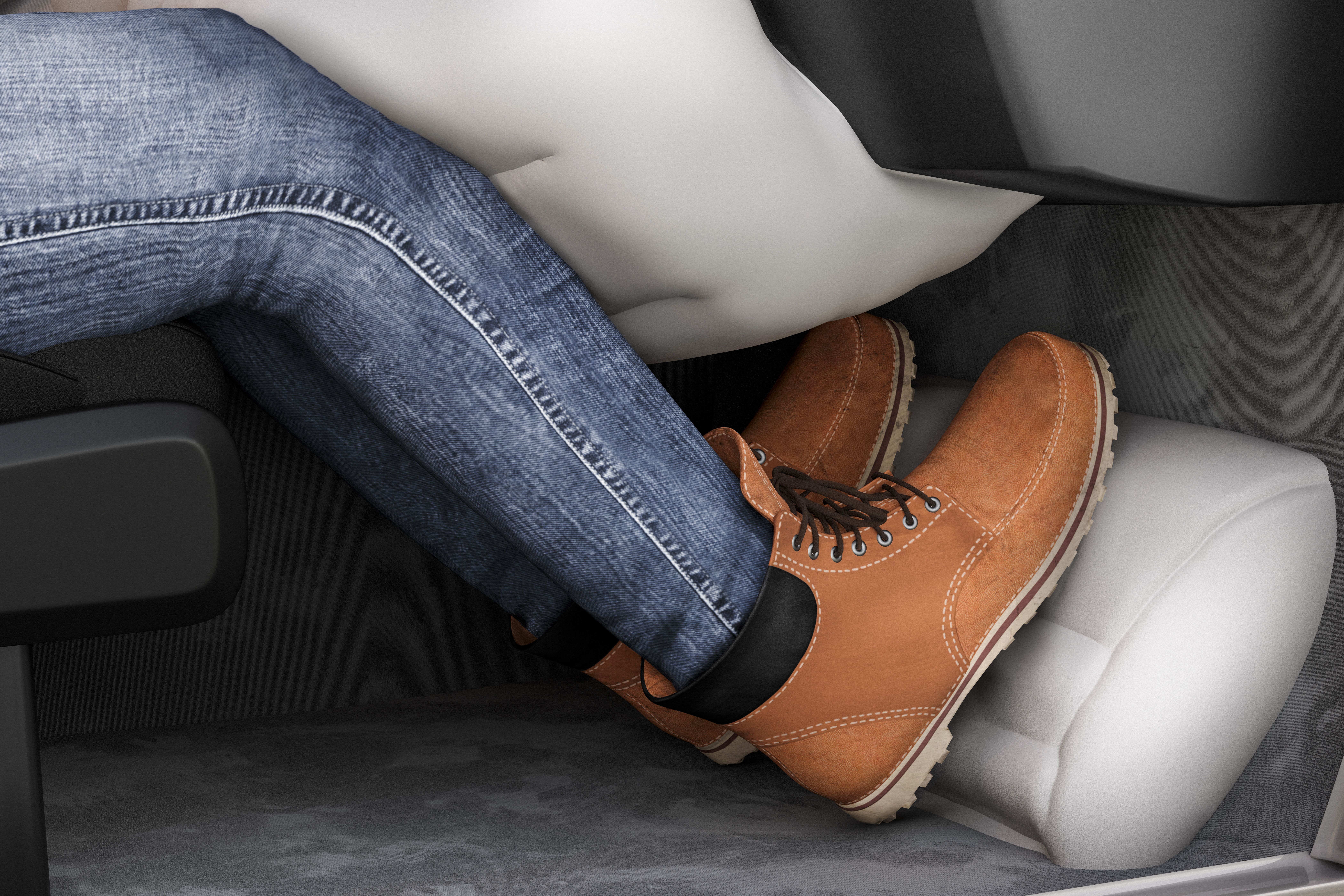 A close-up image of a person's legs wearing blue jeans and brown boots, with feet resting on an inflated heel airbag under the dashboard of a vehicle.